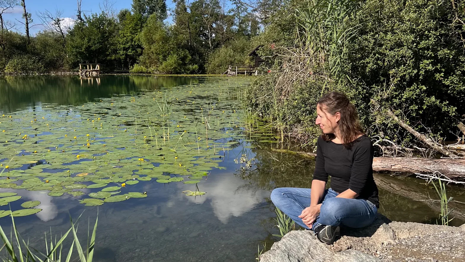 Jeannine Maurer sitzt stressfrei im Schneidersitz auf einem grossen Stein direkt am Wasser