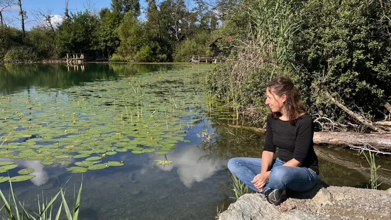 Jeannine Maurer sitzt stressfrei im Schneidersitz auf einem grossen Stein direkt am Wasser